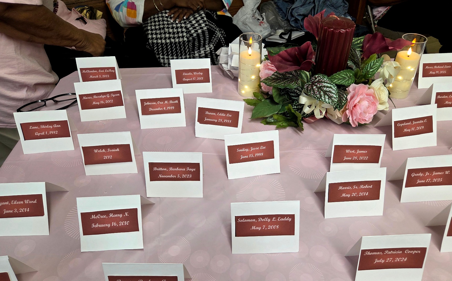 Memorial name cards arranged around flowers and candles on a remembrance table.